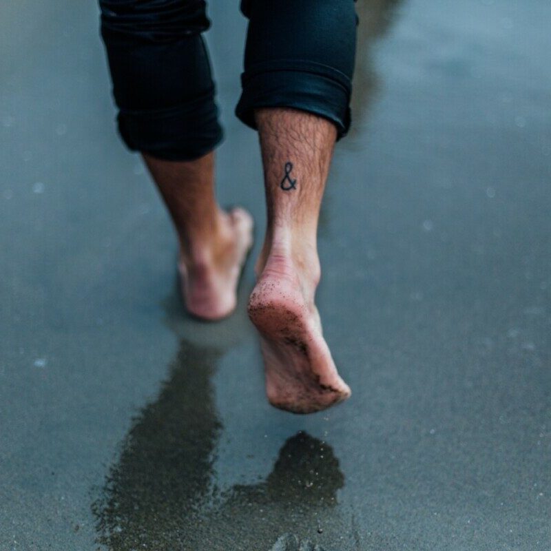 person with tattoo on foot walking on wet sands